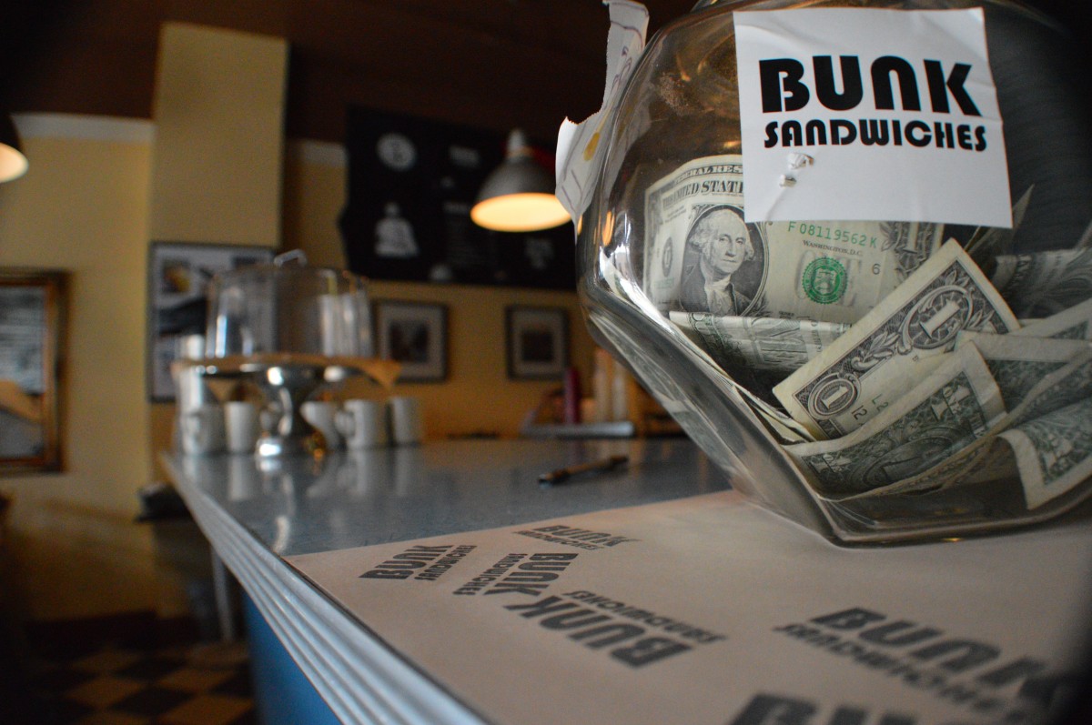 A neighborhood bar counter with a tip jar and seating in the background.