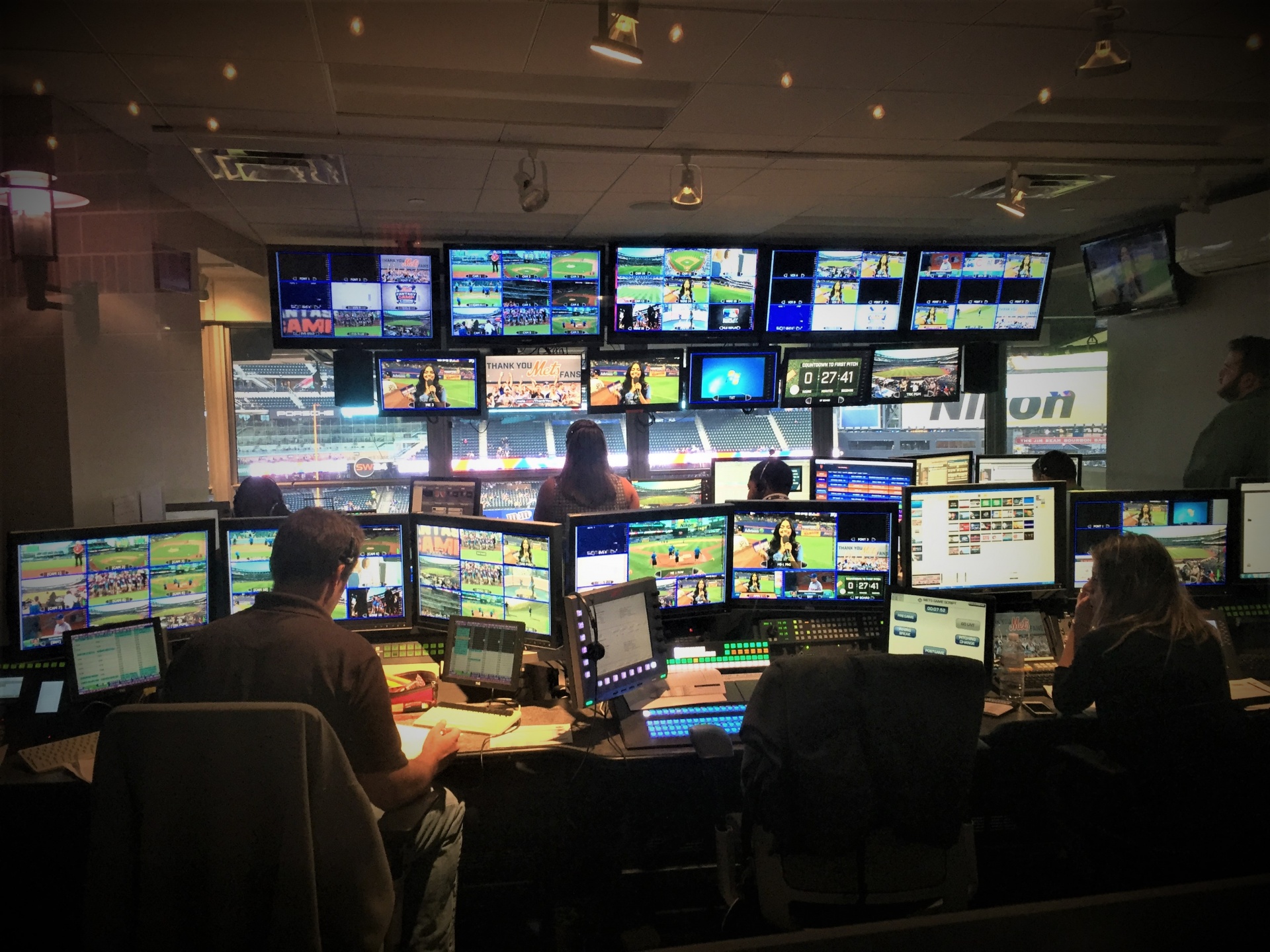 Staff monitor game broadcasts from a stadium control room.